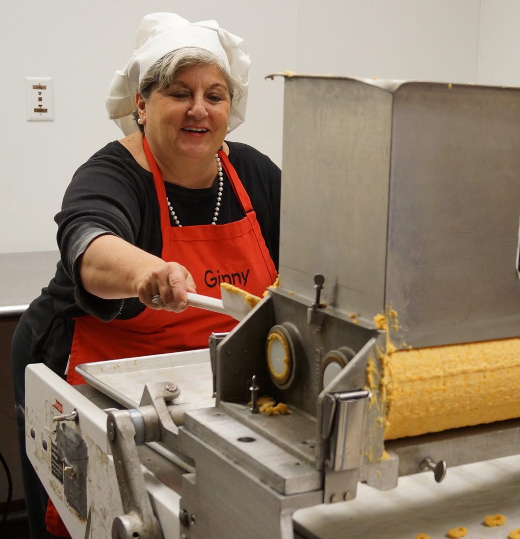 Ginny Johnson in her chef's hat and red apron, working the dough press